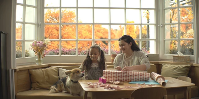 Madre e hija sentadas en una sala de estar con su perro envolviendo regalos