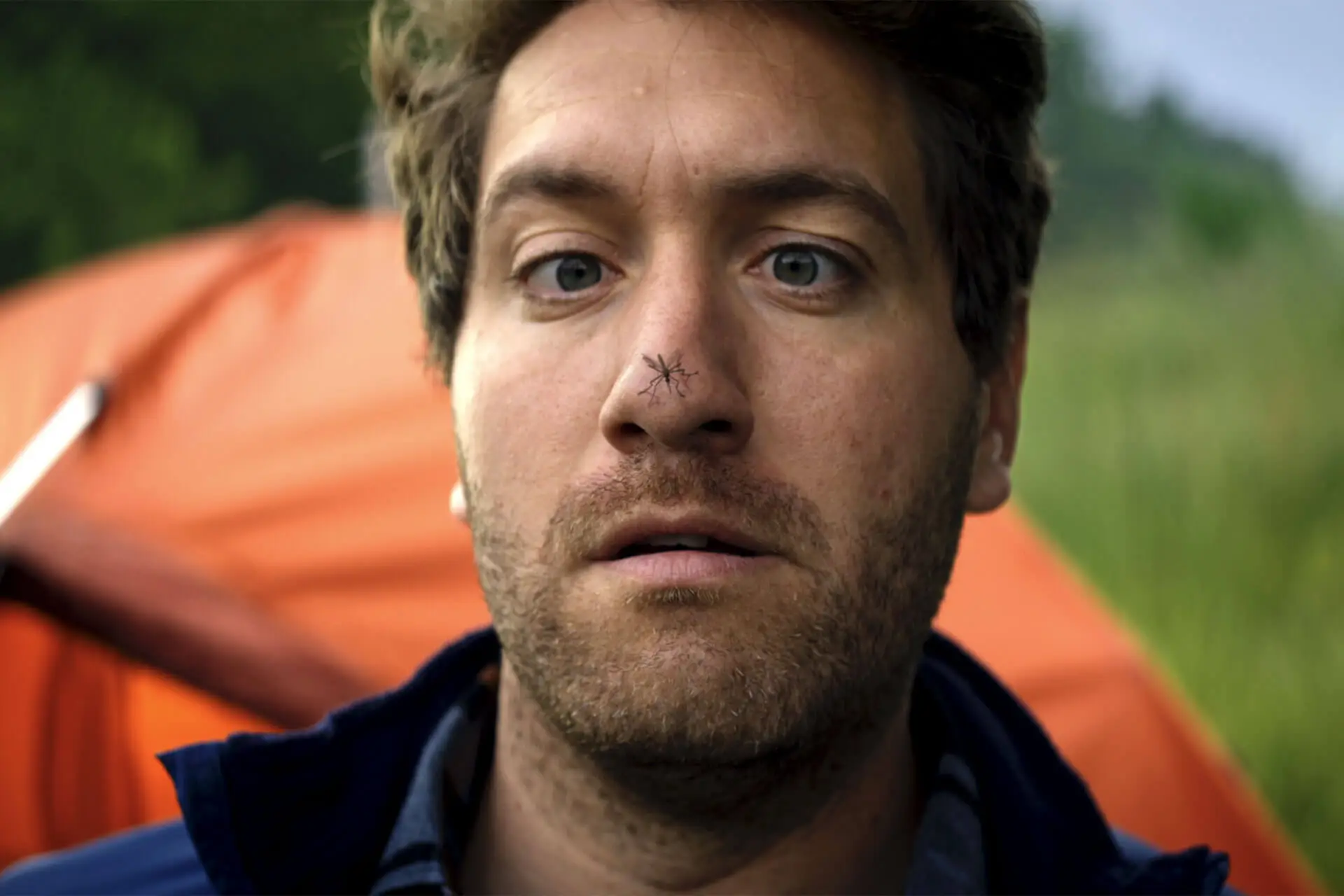 Man camping with a mosquito on his nose